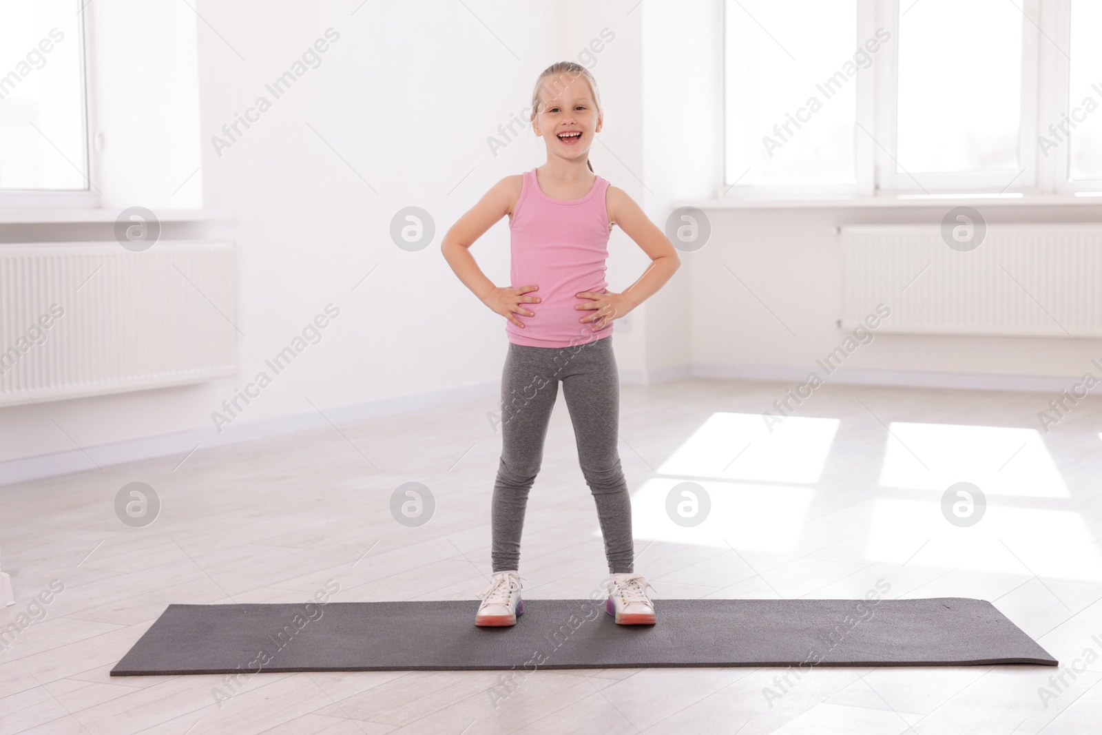 Happy girl standing on yoga mat indoors Photo of Happy girl standing on yoga mat indoors