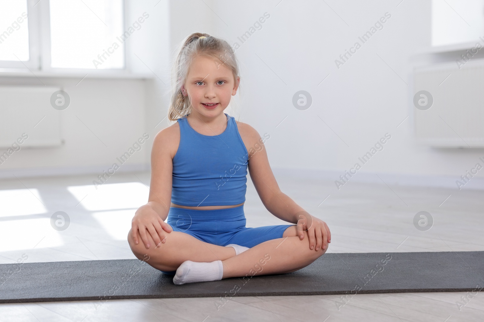 Happy girl sitting on yoga mat indoors Photo of Happy girl sitting on yoga mat indoors