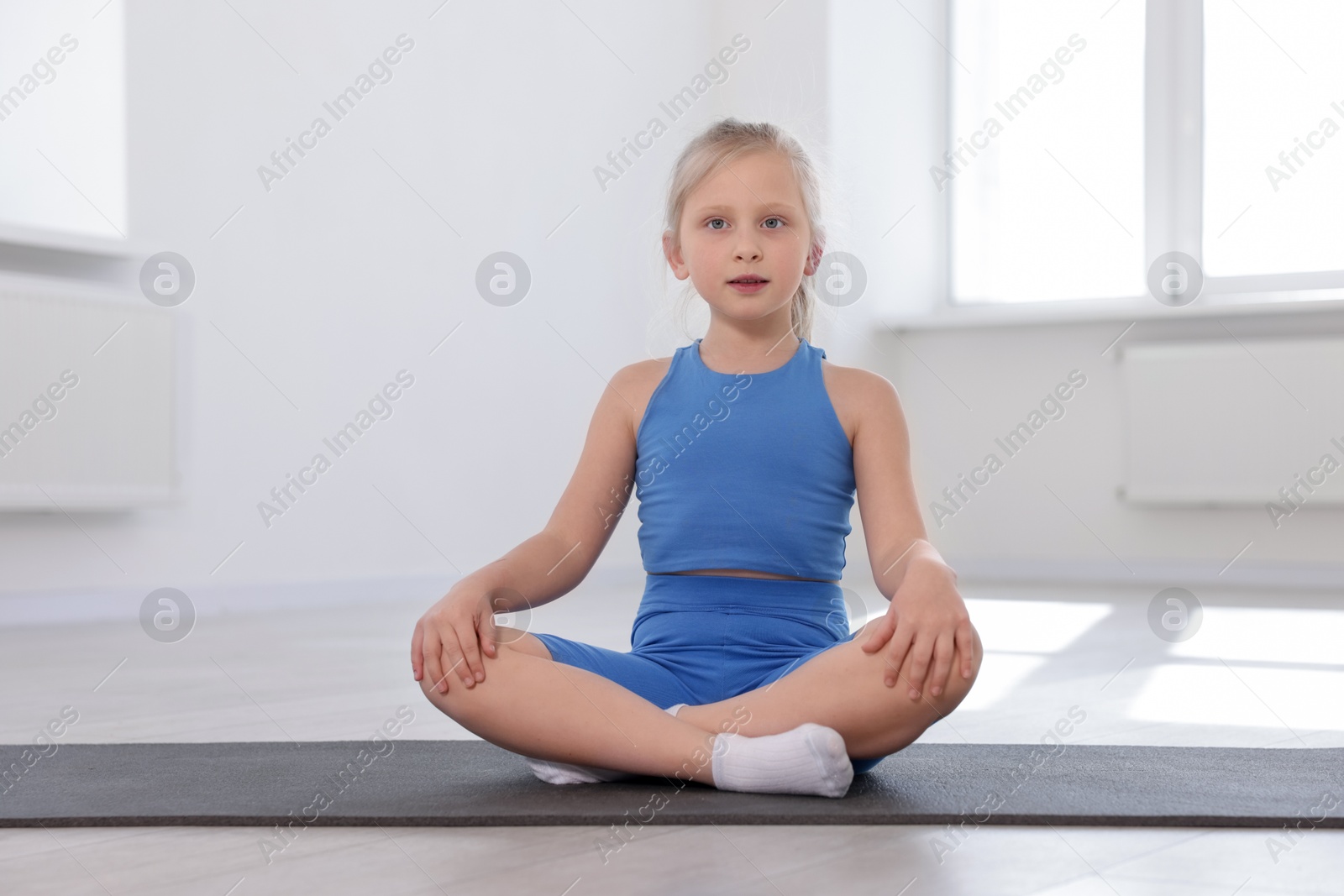 Cute girl sitting on yoga mat indoors Photo of Cute girl sitting on yoga mat indoors