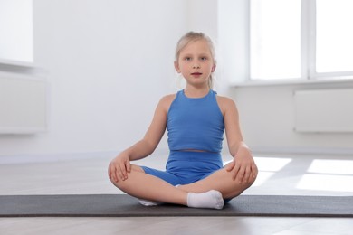Photo of Cute girl sitting on yoga mat indoors