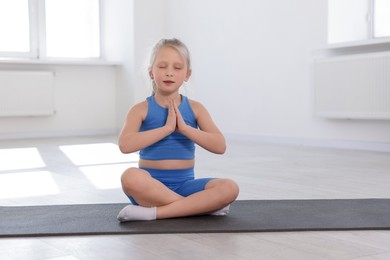 Photo of Cute girl meditating on yoga mat indoors