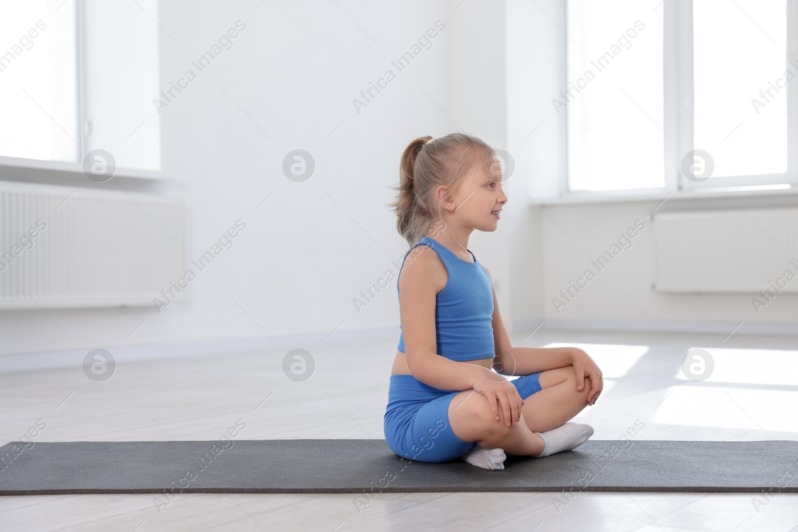 Cute girl sitting on yoga mat indoors Photo of Cute girl sitting on yoga mat indoors