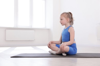 Photo of Cute girl sitting on yoga mat indoors