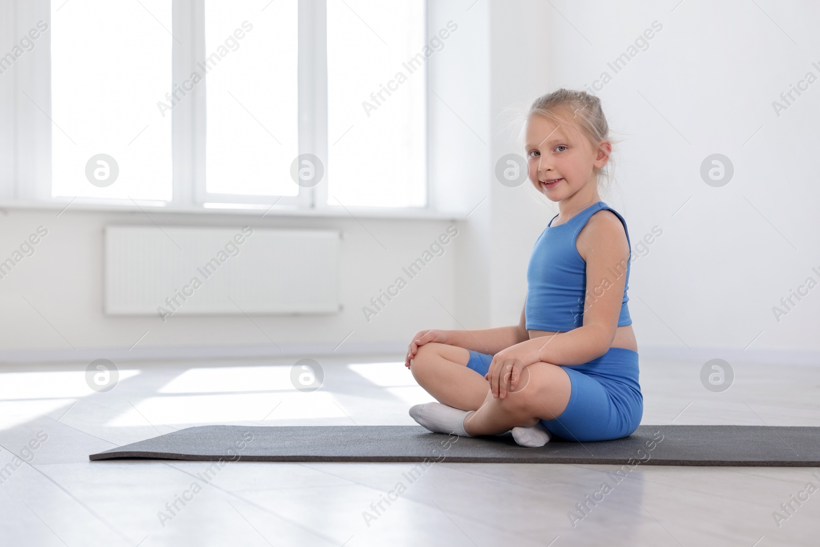 Happy girl sitting on yoga mat indoors Photo of Happy girl sitting on yoga mat indoors