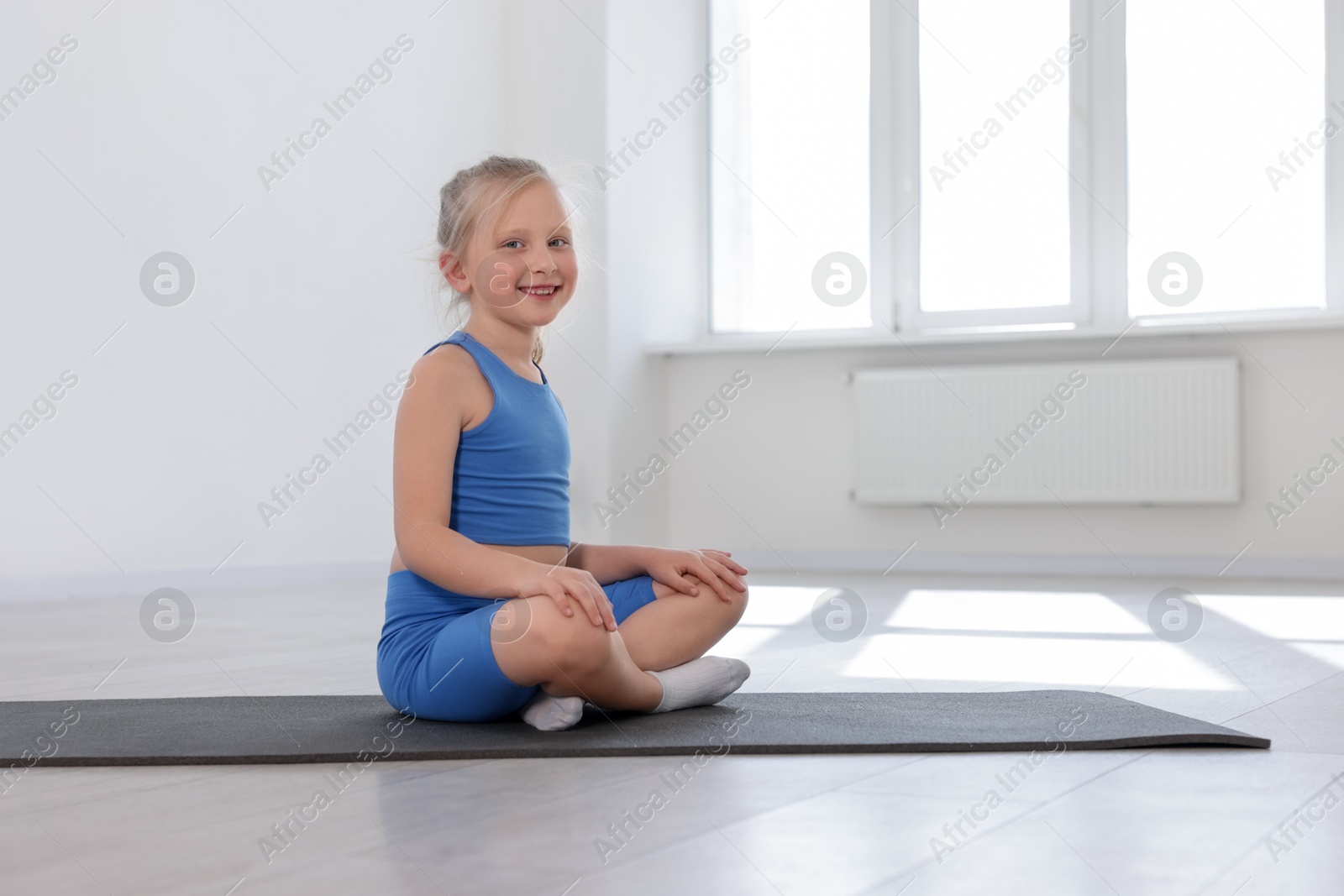Happy girl sitting on yoga mat indoors Photo of Happy girl sitting on yoga mat indoors