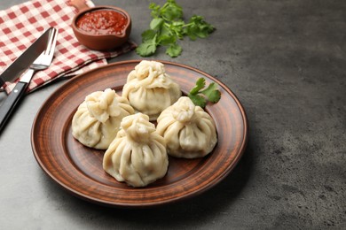 Photo of Delicious khinkali served with sauce on grey table, closeup