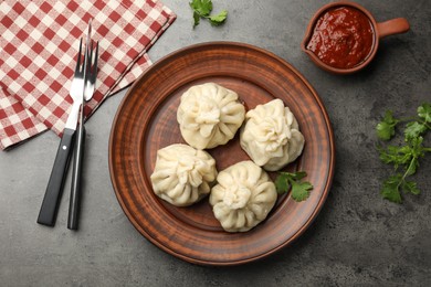 Photo of Delicious khinkali served with sauce on grey table, flat lay