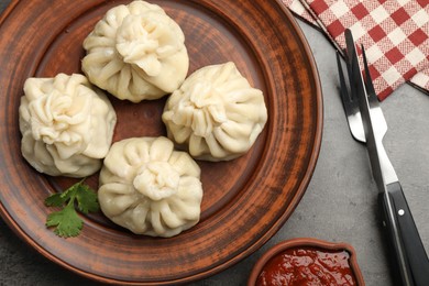 Photo of Delicious khinkali served with sauce on grey table, flat lay