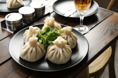Photo of Delicious khinkali served with cilantro and wine on wooden table, closeup