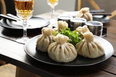 Photo of Delicious khinkali served with cilantro and wine on wooden table, closeup