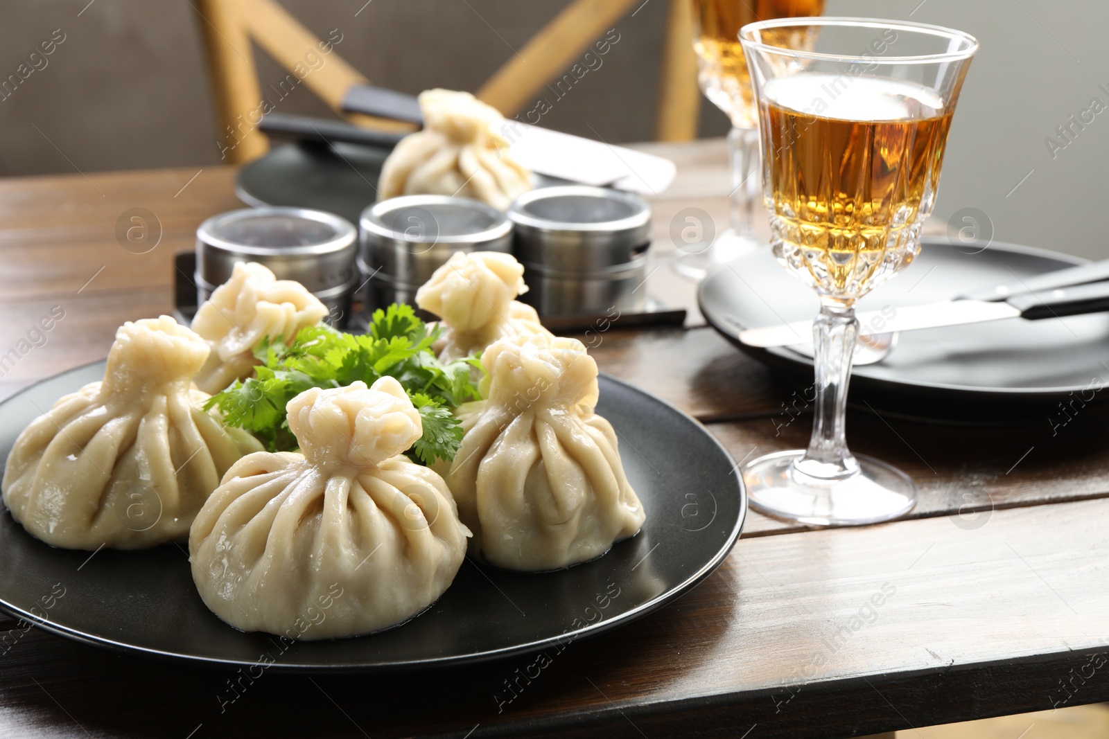 Photo of Delicious khinkali served with cilantro and wine on wooden table, closeup