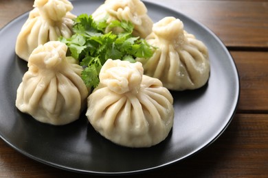 Photo of Delicious khinkali served with cilantro on wooden table, closeup