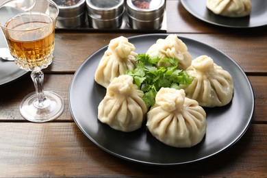 Photo of Delicious khinkali served with cilantro and wine on wooden table, closeup