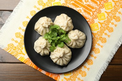 Photo of Delicious khinkali served with cilantro on wooden table, top view