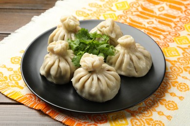 Photo of Delicious khinkali served with cilantro on wooden table, closeup