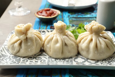 Photo of Delicious cooked khinkali served with sauce on grey table, closeup
