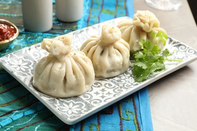 Photo of Delicious khinkali served with sauce and cilantro on grey table, closeup