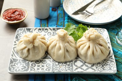 Photo of Delicious khinkali served with sauce and cilantro on grey table, closeup