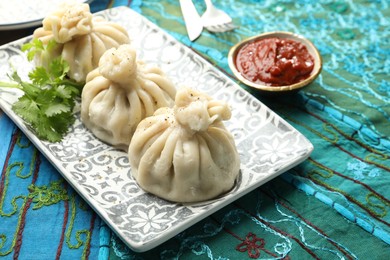 Photo of Delicious khinkali served with sauce and cilantro on table, closeup
