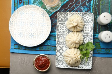 Photo of Delicious khinkali served with sauce and cilantro on grey table, flat lay