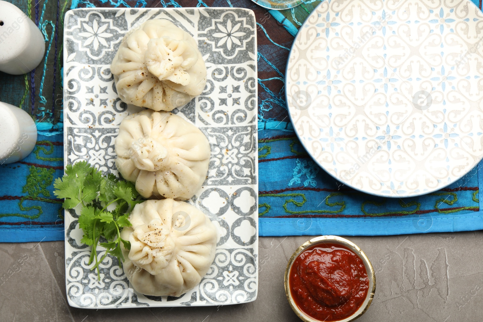 Photo of Delicious khinkali served with sauce and cilantro on grey table, flat lay