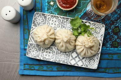 Photo of Delicious khinkali served with sauce and cilantro on grey table, flat lay