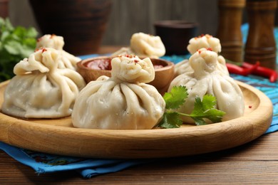 Photo of Delicious khinkali served with sauce on wooden table, closeup