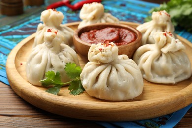Photo of Delicious khinkali served with sauce on wooden table, closeup
