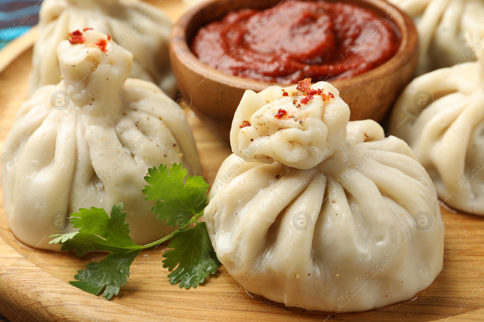 Delicious khinkali served with sauce on wooden plate, closeup Photo of Delicious khinkali served with sauce on wooden plate, closeup