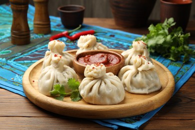 Photo of Delicious khinkali served with sauce on wooden table, closeup