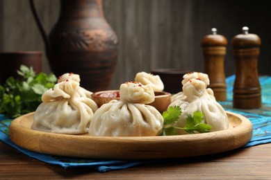 Photo of Delicious khinkali served with sauce on wooden table, closeup