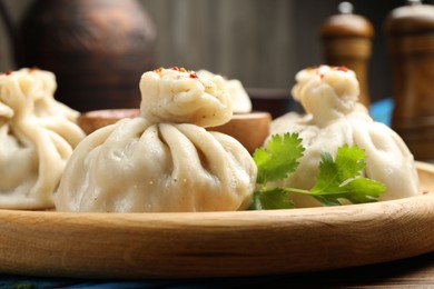 Photo of Delicious khinkali served with sauce on wooden plate, closeup