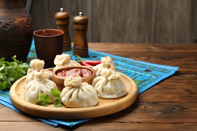 Photo of Delicious khinkali served with sauce on wooden table, closeup