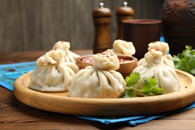 Photo of Delicious khinkali served with sauce on wooden table, closeup
