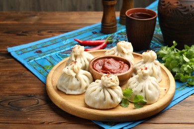 Photo of Delicious khinkali served with sauce on wooden table, closeup