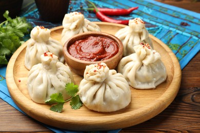 Photo of Delicious khinkali served with sauce on wooden table, closeup