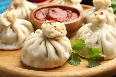Photo of Delicious khinkali served with sauce on wooden plate, closeup