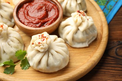 Photo of Delicious khinkali served with sauce on wooden table, closeup
