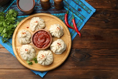 Photo of Delicious khinkali served with sauce on wooden table, flat lay