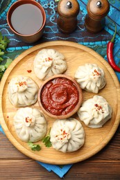 Photo of Delicious khinkali served with sauce on wooden table, flat lay