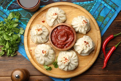 Photo of Delicious khinkali served with sauce on wooden table, flat lay