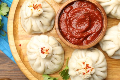 Photo of Delicious khinkali served with sauce on wooden table, top view