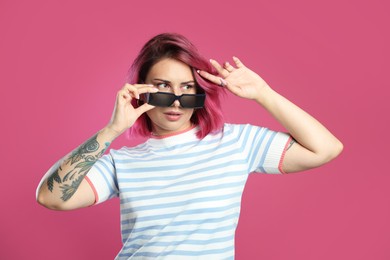 Photo of Beautiful woman with bright dyed hair in sunglasses on pink background