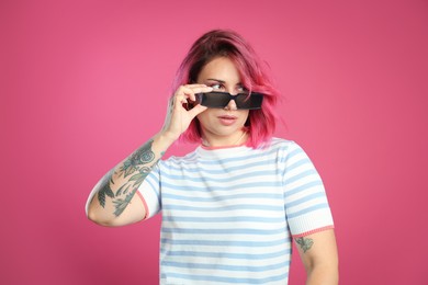 Photo of Beautiful woman with bright dyed hair in sunglasses on pink background
