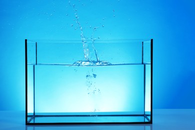 Photo of Glass aquarium with splashing water on table against light blue background