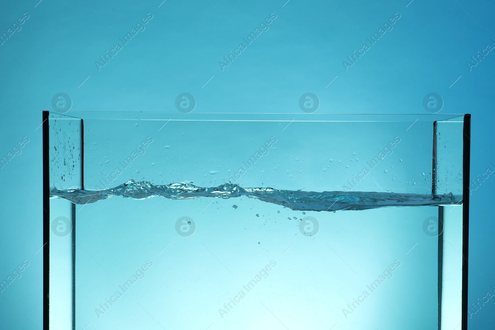 Glass aquarium with splashing water on light blue background, closeup Photo of Glass aquarium with splashing water on light blue background, closeup