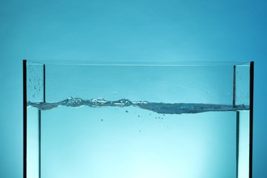 Photo of Glass aquarium with splashing water on light blue background, closeup
