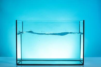 Photo of Glass aquarium with splashing water on table against light blue background