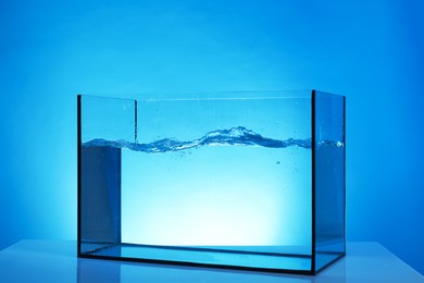 Photo of Glass aquarium with splashing water on table against light blue background
