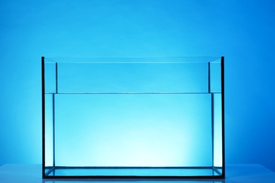 Photo of Glass aquarium with water on table against light blue background